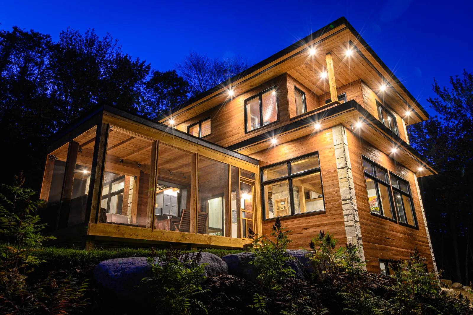 Maison de bois illuminée au crépuscule, réalisation de Canopée Développement