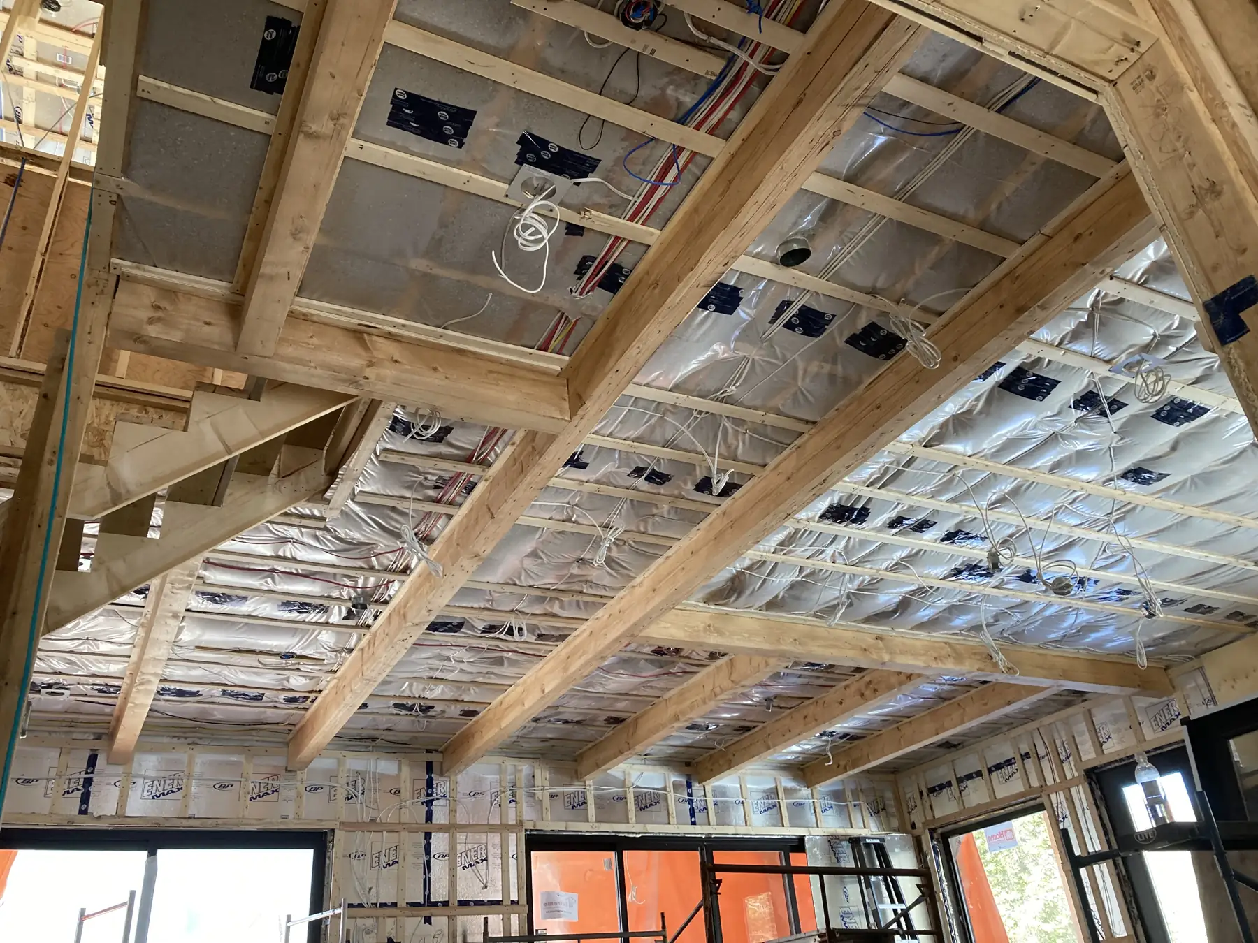 Charpente intérieure en cours : solives de bois apparentes, isolation réfléchissante et conduits électriques, grandes ouvertures au fond