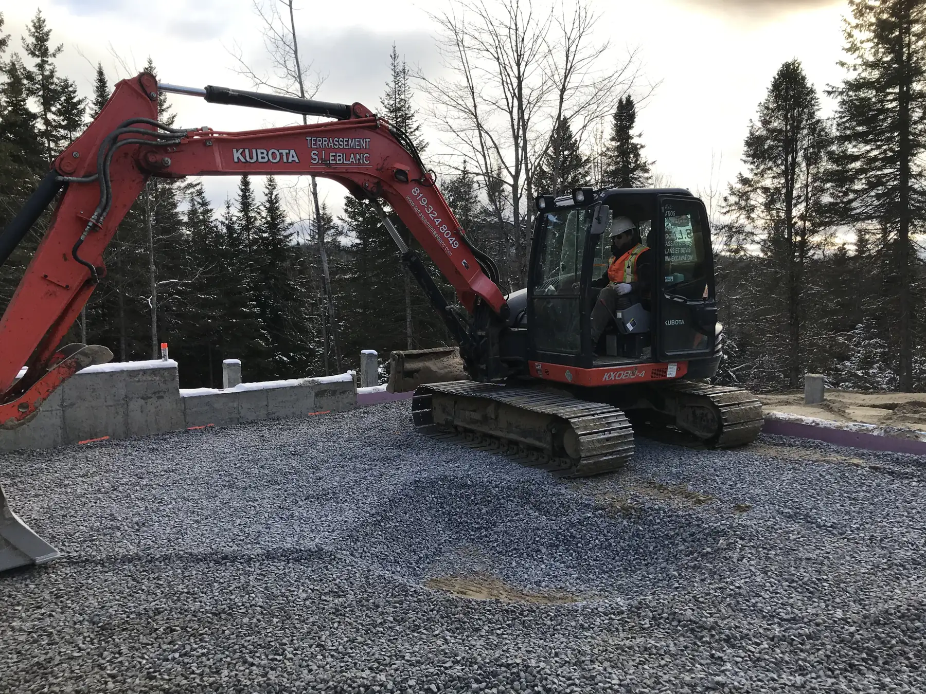 Pelle mécanique sur chenilles répartissant la pierre concassée à l'intérieur des fondations de béton d'une résidence en construction